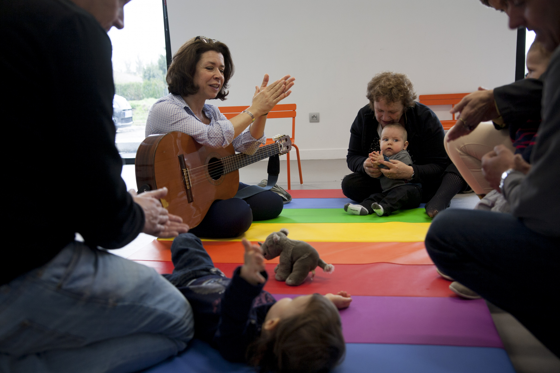 Une dame avec une guitare regarde un bébé sur un tapis
